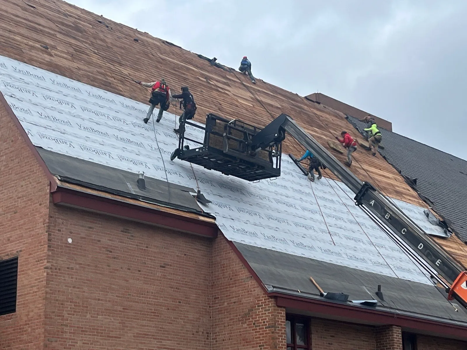 Above Roofing crew in harnesses on rope lines installing underlayment on the pitched sanctuary roof of Calvin Christian Reformed Church in Grand Rapids